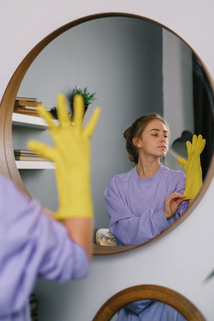 project-01-b A woman wearing yellow gloves is reflected in a wall mirror indoors, exuding a serene expression.